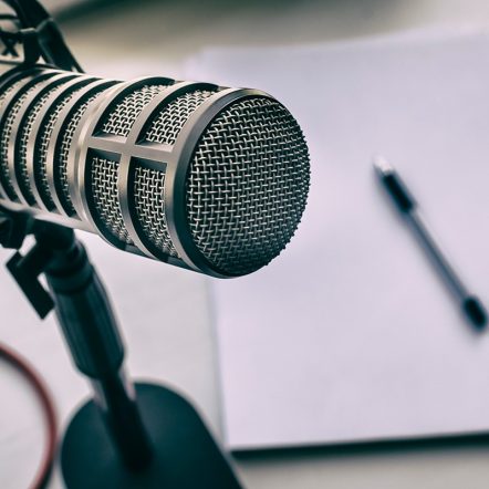 silver metal microphone and a pen and a paper at the blurred background, indicating a podcast
