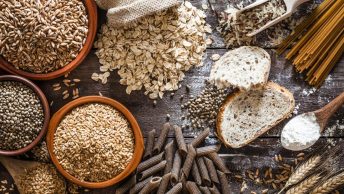 A bunch of carbohydrates, such as oats, whole grain pasta, bread and quinoa on a wooden table